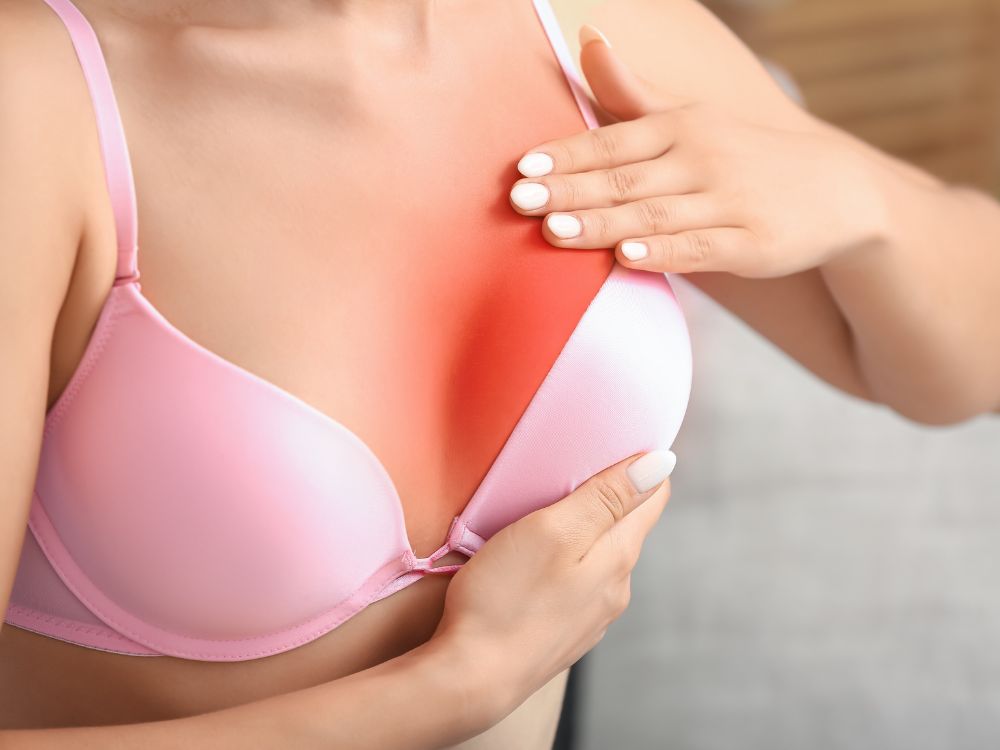 Mulher com dor na mama após mamoplastia redutora. Inflamação e cicatrização podem causar desconforto no pós-operatório.