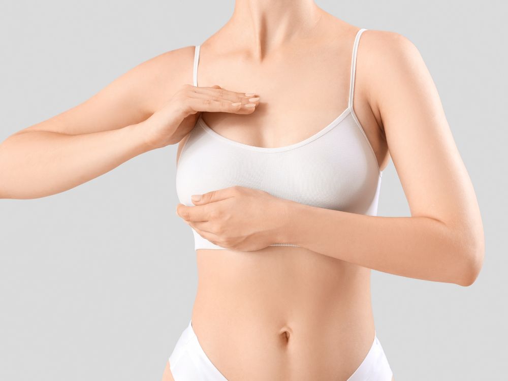 Mulher tocando os seios antes da cirurgia plástica. Saiba mais sobre mamoplastia redutora risco de morte e como garantir um procedimento seguro.