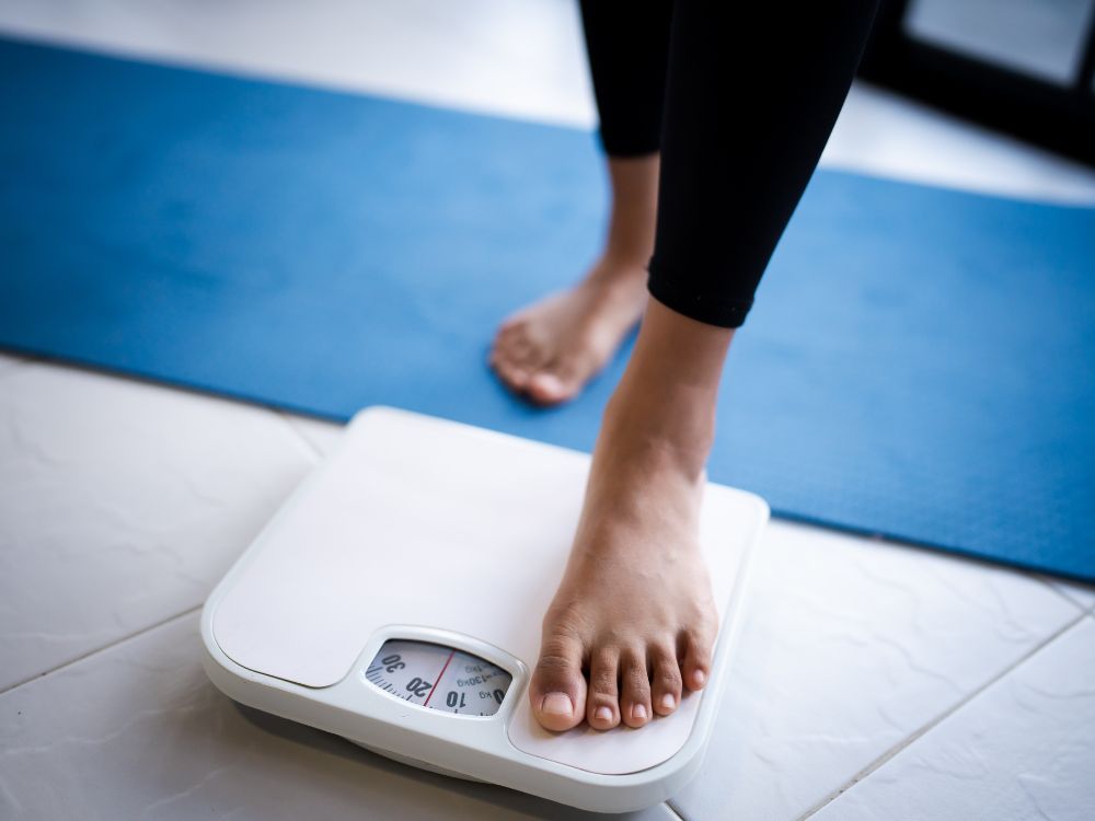 Pessoa se pesando em balança: Lipoaspiração emagrece visualmente, mas o impacto na balança costuma ser mínimo.