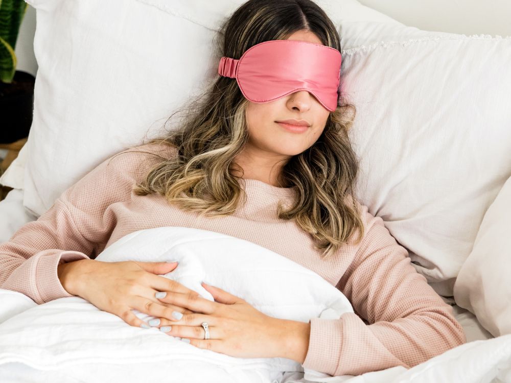 Mulher deitada com máscara de dormir e coberta até a cintura, em posição adequada sobre como dormir após a mamoplastia redutora com segurança.