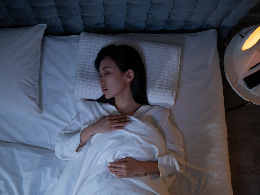 Mulher dormindo de barriga para cima com travesseiro ortopédico, posição ideal recomendada sobre como dormir após a mamoplastia redutor