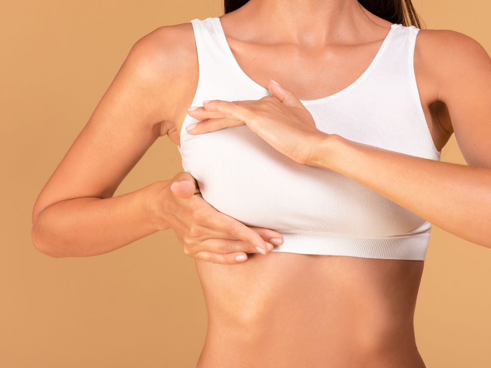 Mulher com top branco realizando exame nos seios, representando cuidados relacionados a o que é mamoplastia.