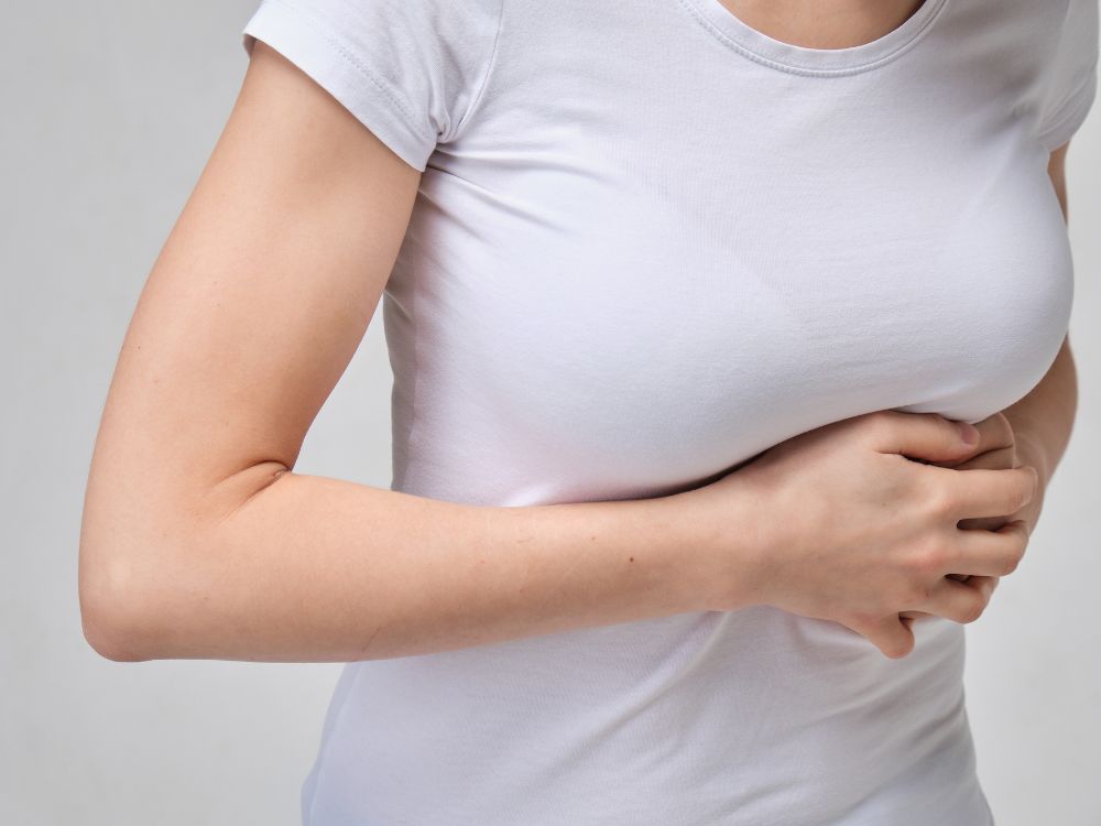 Paciente segurando a mama com expressão de incômodo, exemplificando fisgadas na mama após cirurgia no pós-operatório.