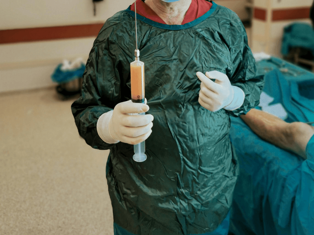 Profissional em ambiente cirúrgico segura seringa durante etapa de preparação para procedimento estético abdominal.