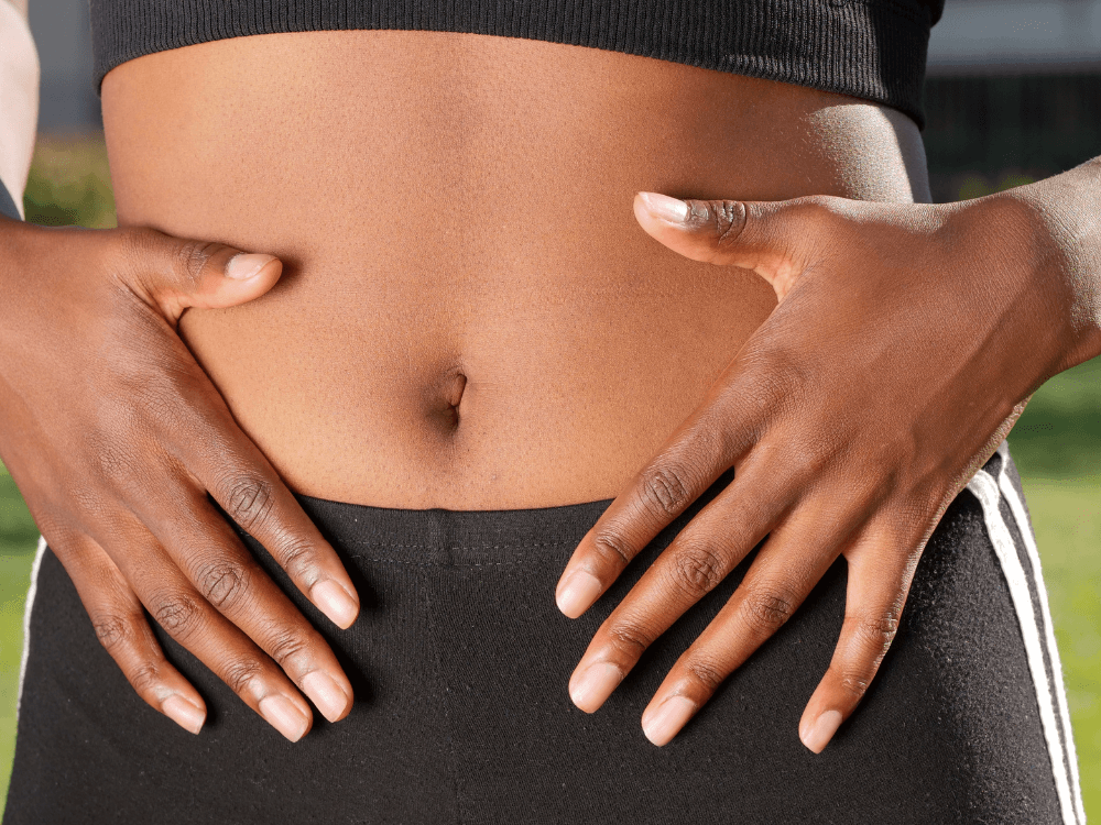 Pessoa com as mãos sobre o abdômen, destacando o contorno abdominal obtido após o período de recuperação da cirurgia.