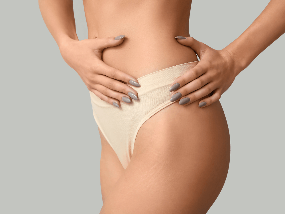 Mulher toca a região abdominal coberta por cinta, representando o cuidado com o corpo após procedimentos estéticos.