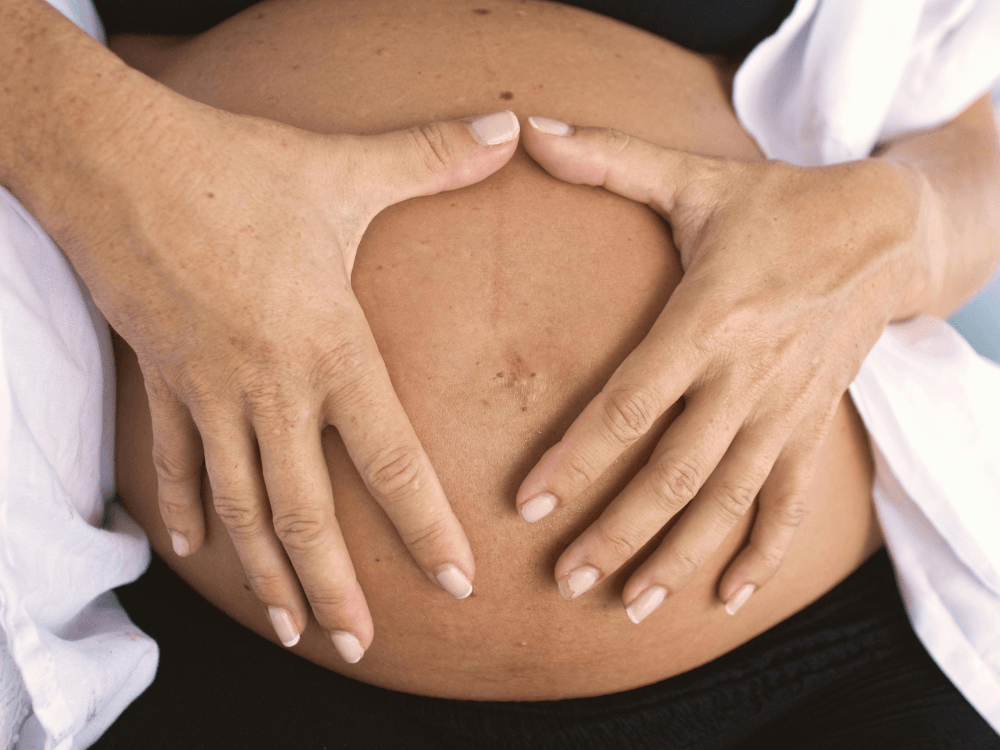 Pessoa segura a região do abdômen com as duas mãos, destacando a área corporal relacionada à abdominoplastia.