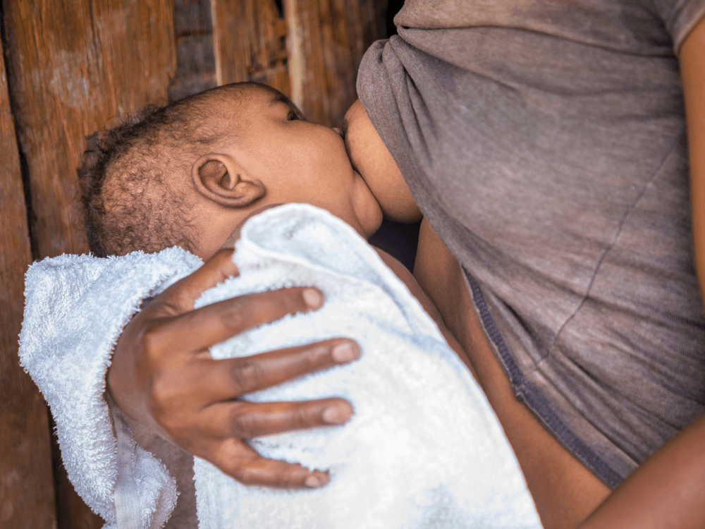 Mãe negra amamenta bebê no colo, em ambiente doméstico, ilustrando dúvidas sobre amamentação após implante mamário.