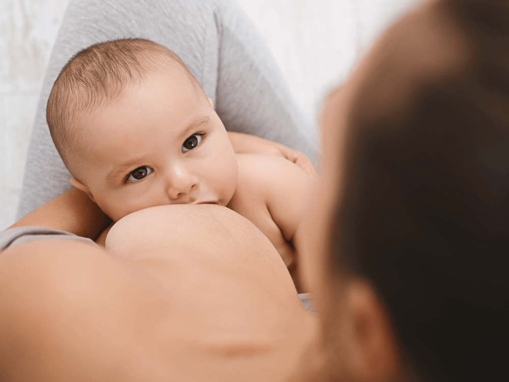 Mãe amamenta bebê que está mamando no peito, em imagem que representa a relação entre silicone e amamentação. Tudo para explicar se quem tem silicone pode amamentar.